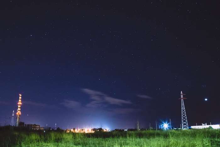 Night sky with stars over industrial landscape and power lines