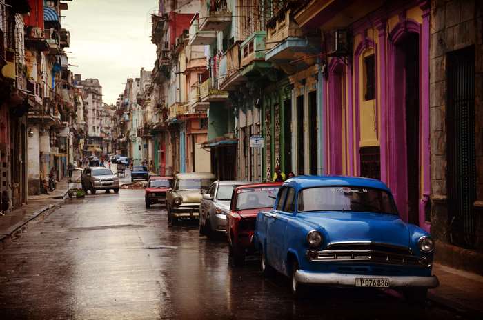 Vintage cars parked on a wet street in a colorful city