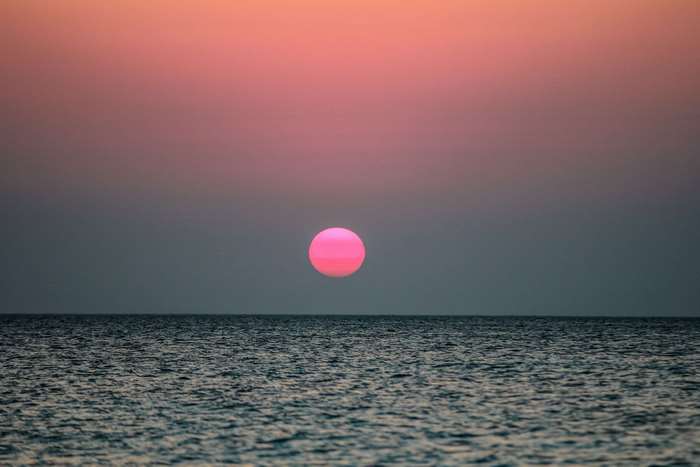 Pink sun setting over the ocean horizon