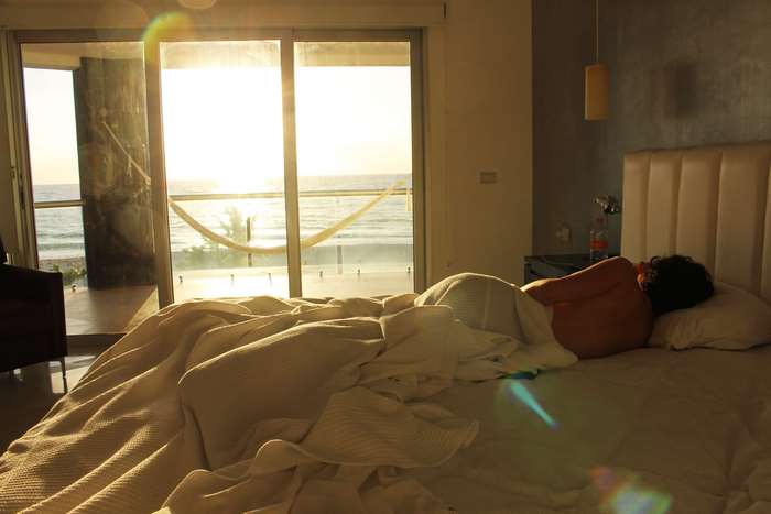 Person sleeping in bed by the ocean at sunrise
