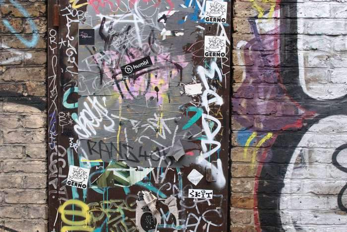Graffiti and stickers on a metal door and brick wall in Shoreditch