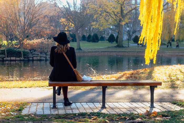 Woman in hat sitting on park bench by lake in fall