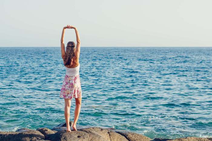 Woman stretching arms by the ocean on rocks