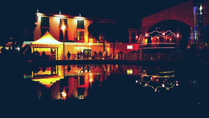 Night festival with illuminated tents and stage reflected in water