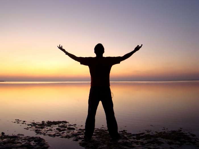 Silhouette of a man with arms raised at sunset over water