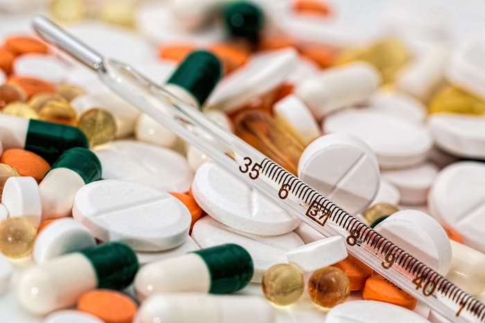 Pile of pills and capsules with a thermometer
