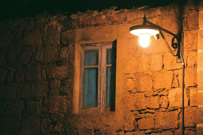 Old stone house with a window and a lamp at night