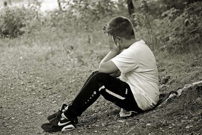 Boy sitting alone in nature, covering face