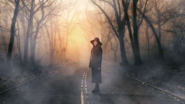 Girl in a hat on a foggy road in a forest