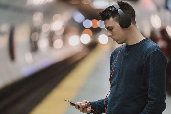 Man wearing headphones and looking at smartphone at station