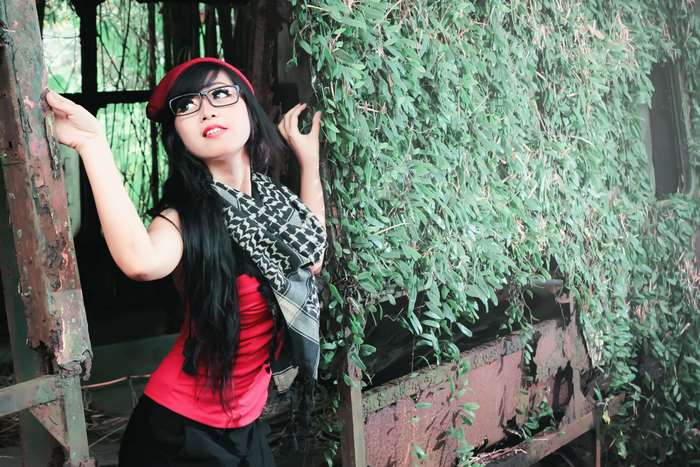 Young woman in red top and beret posing near overgrown rusty structure