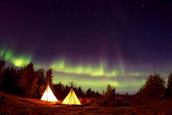 Teepees under the Aurora Borealis in a forest at night
