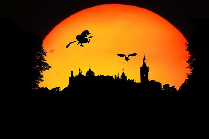 Silhouette of a witch flying on a broomstick with an owl over a castle at sunset