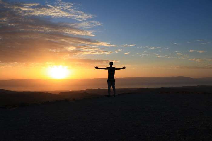 Person with arms outstretched at sunrise over a landscape