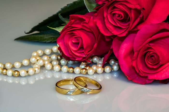Gold wedding rings with diamonds, pearls, and red roses 4K