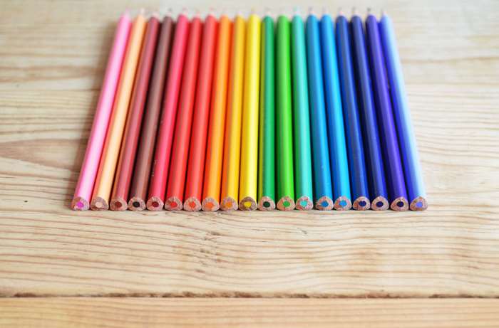Colored pencils arranged in a rainbow on a wooden surface