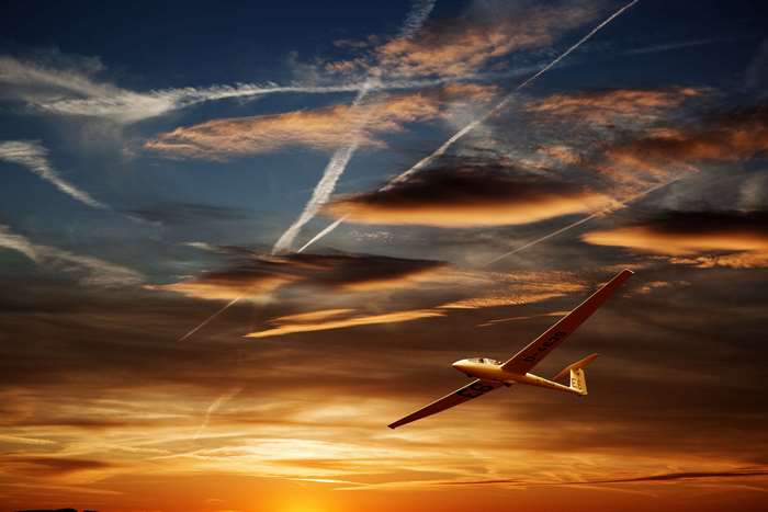 Glider flying at sunset with contrails