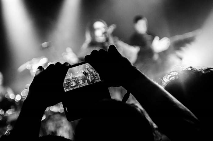 Person filming a band performing on stage at a concert