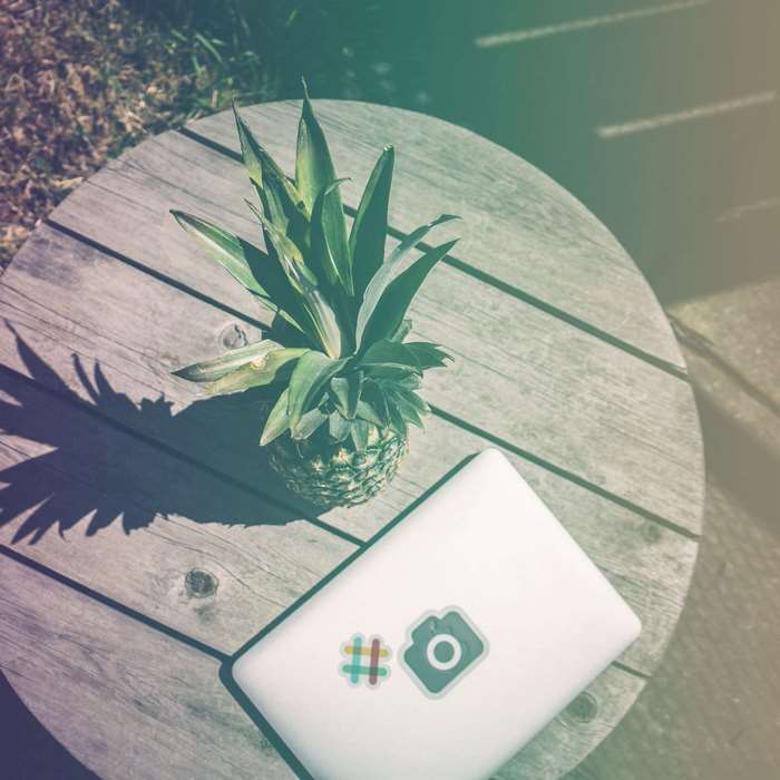 Pineapple and laptop with stickers on a wooden table