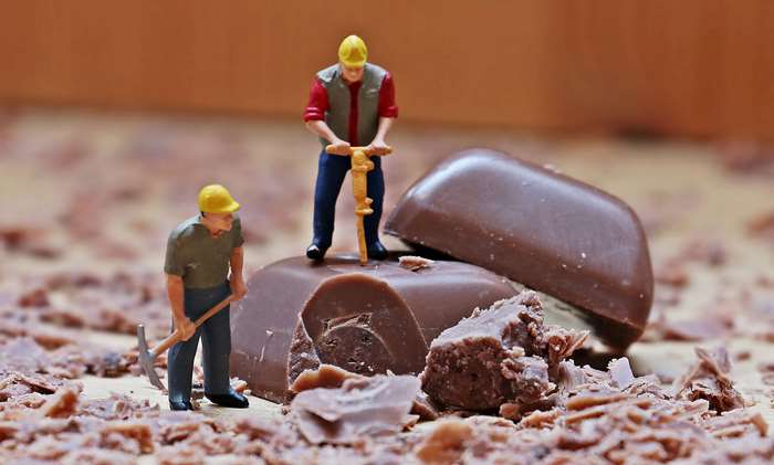 Miniature construction workers breaking chocolate