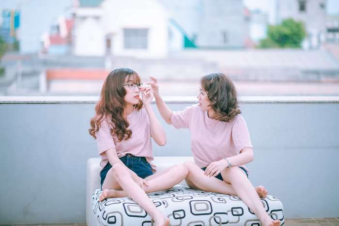 Two young women in pink t-shirts sitting on a patterned bench