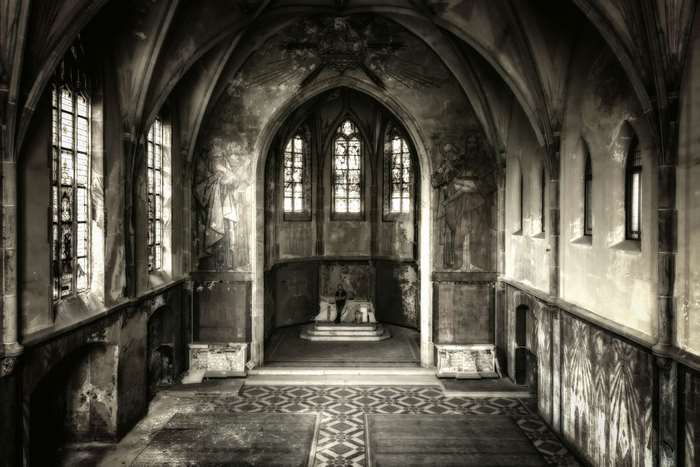 Interior of a decaying chapel with stained glass windows and murals