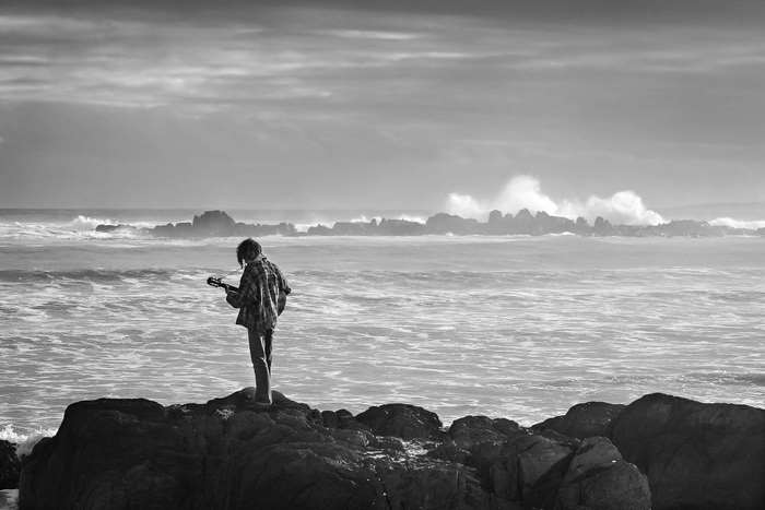 Man playing guitar on rocks by the sea