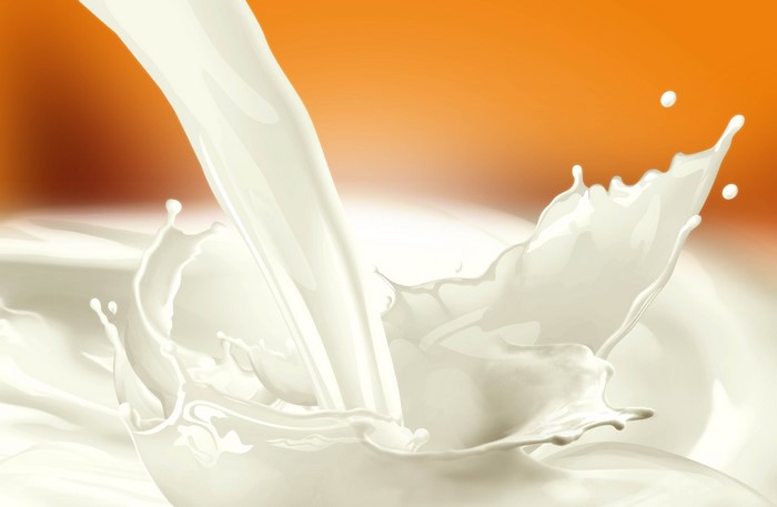 Milk stream splashing on orange background