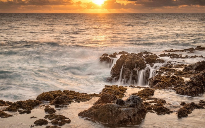 Ocean waves crashing on rocky shore at sunset