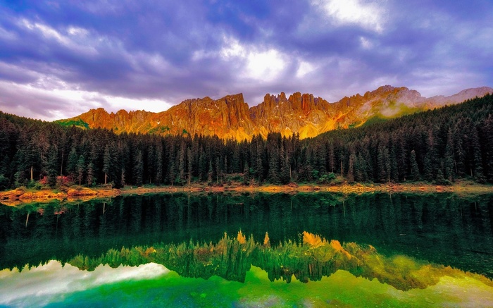 Lake reflecting mountains and forest under dramatic sky