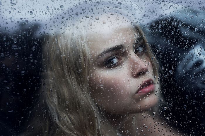Girl looking through a rain-covered window