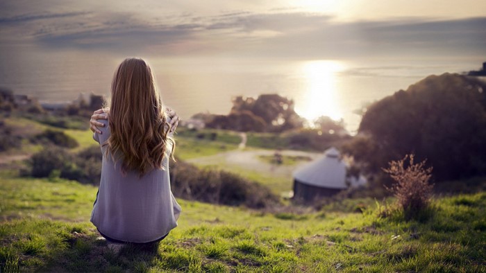 Girl Sitting on Grass Watching Sunset Over Landscape