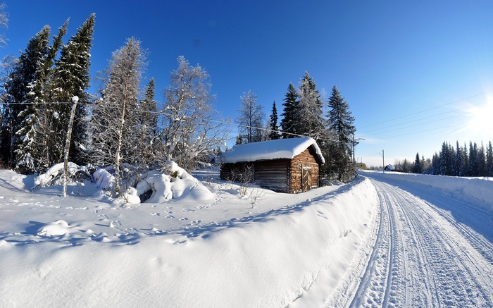 Snowy road next to a wooden cabin in winter