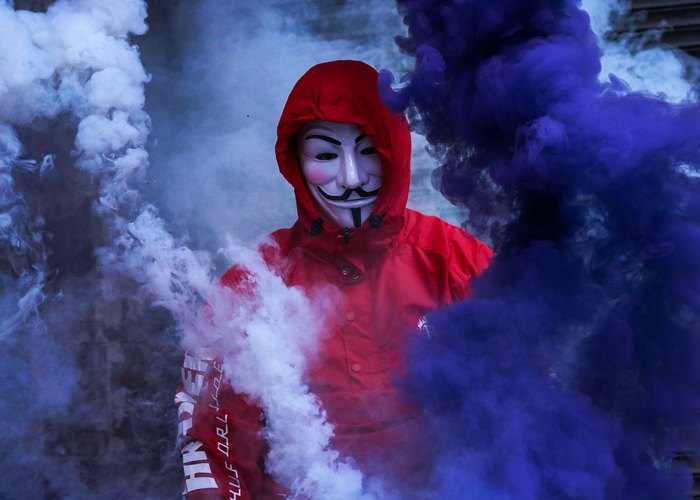 Person in Guy Fawkes mask with smoke bombs
