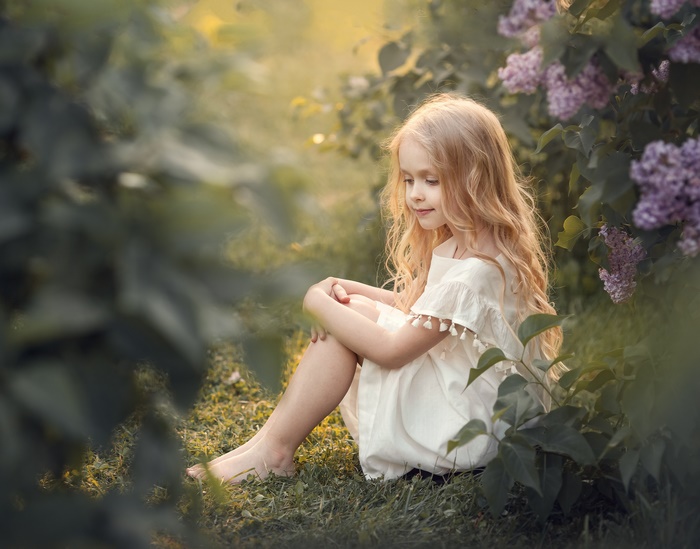 Blonde Little Girl Sitting in Garden with Flowers