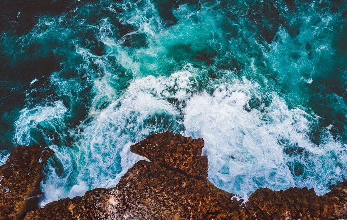 Aerial view of ocean waves crashing on a rocky cliff