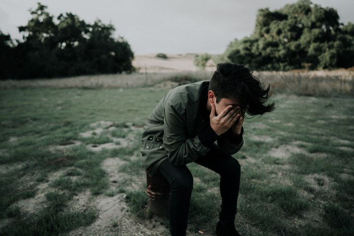 Man sitting in a field covering his face