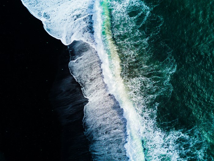 Aerial view of waves crashing on a black sand beach