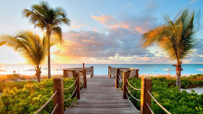 Wooden boardwalk to a tropical beach at sunset
