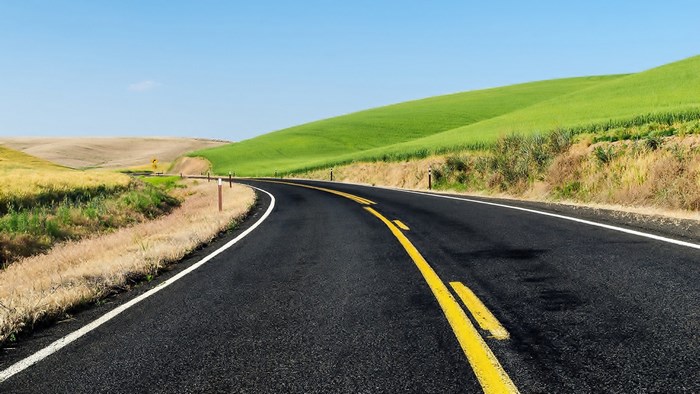Curving asphalt road through rolling green hills