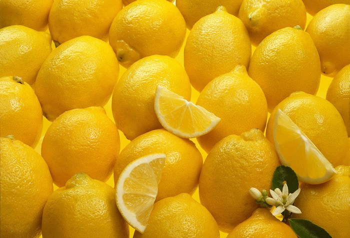 A pile of fresh lemons with slices and a flower