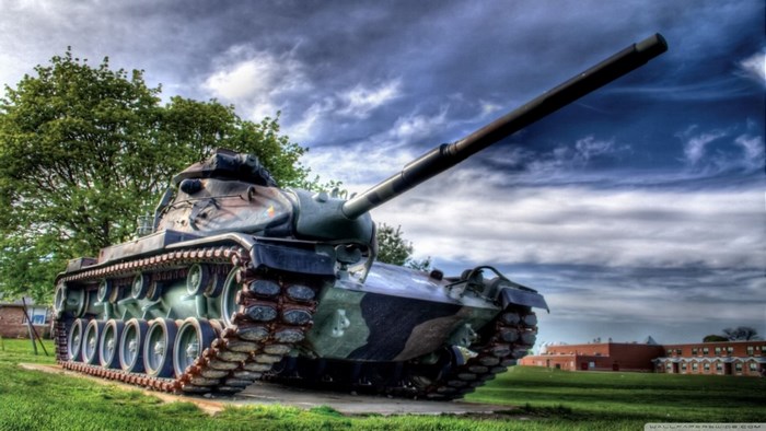 Tank in a grassy field with trees and buildings