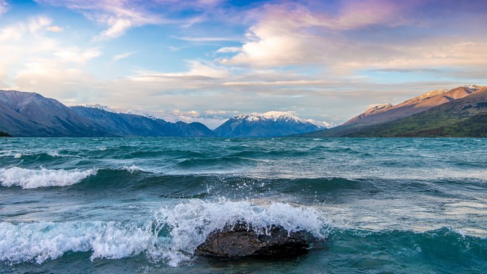 Waves crashing on a rock in a lake with mountains