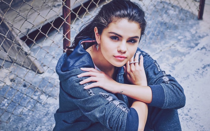 Selena Gomez sitting by a fence