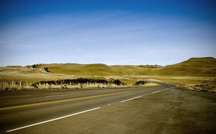 Winding road through rolling hills under a blue sky