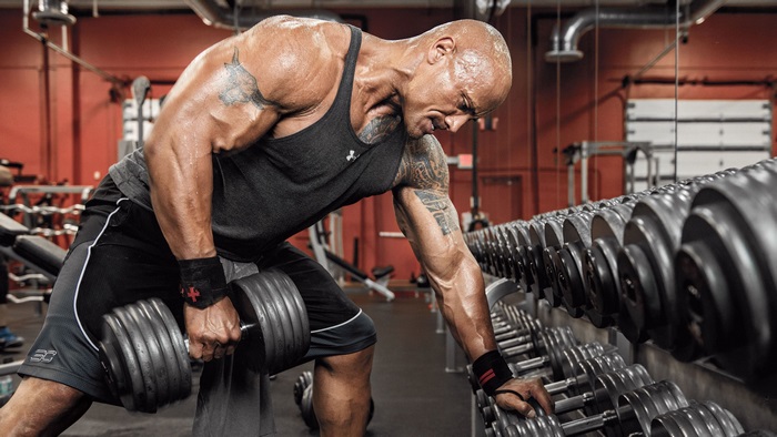 Dwayne Johnson performing dumbbell rows in a gym