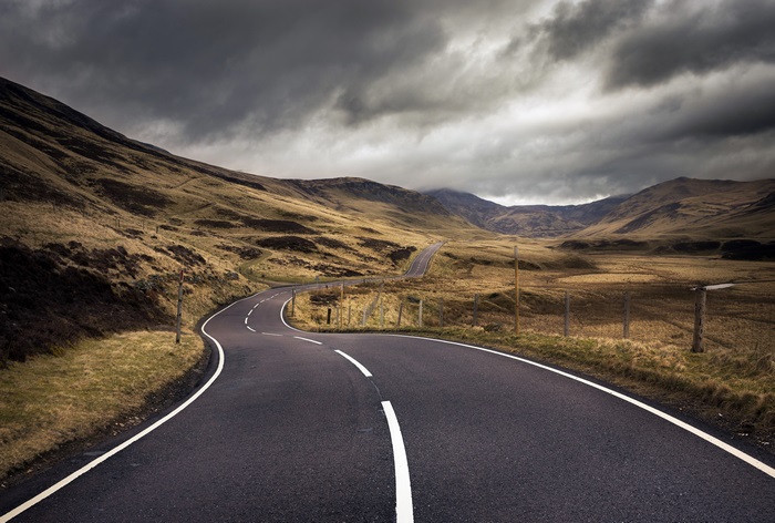 Winding road through a desolate landscape under stormy skies