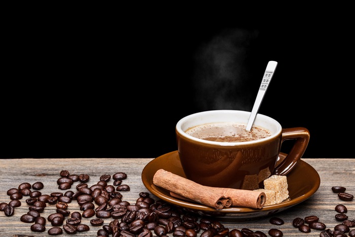 Coffee cup with steam, coffee beans, cinnamon, and sugar cubes