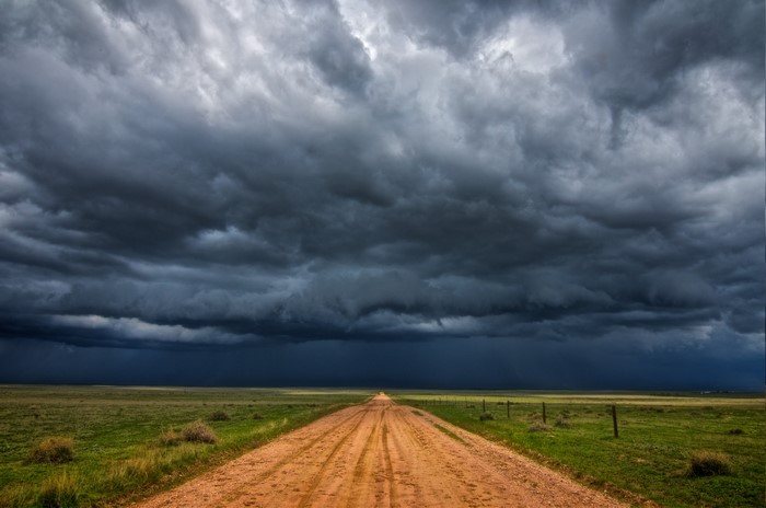 Dirt road leading to a storm under a cloudy sky