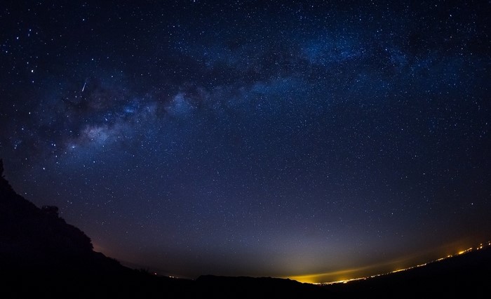 Milky Way galaxy over a dark landscape with city lights
